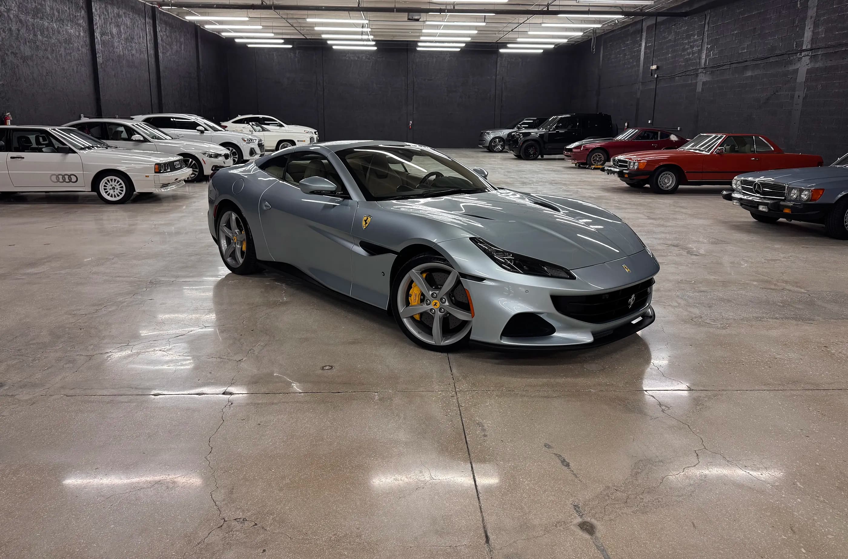 A silver Ferrari Portofino on the polished floor of the Full Stop Garage storage facility, with stored classics and SUVs along the walls behind it